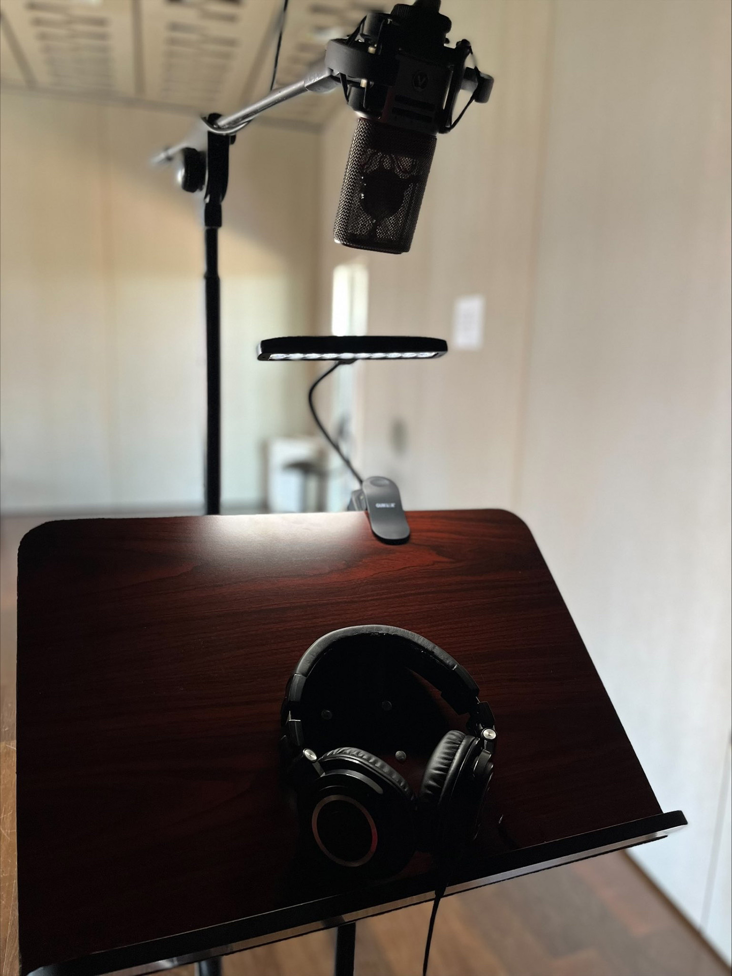 Cuffie e microfono appoggiati su di un leggio di legno illuminato da una lapada