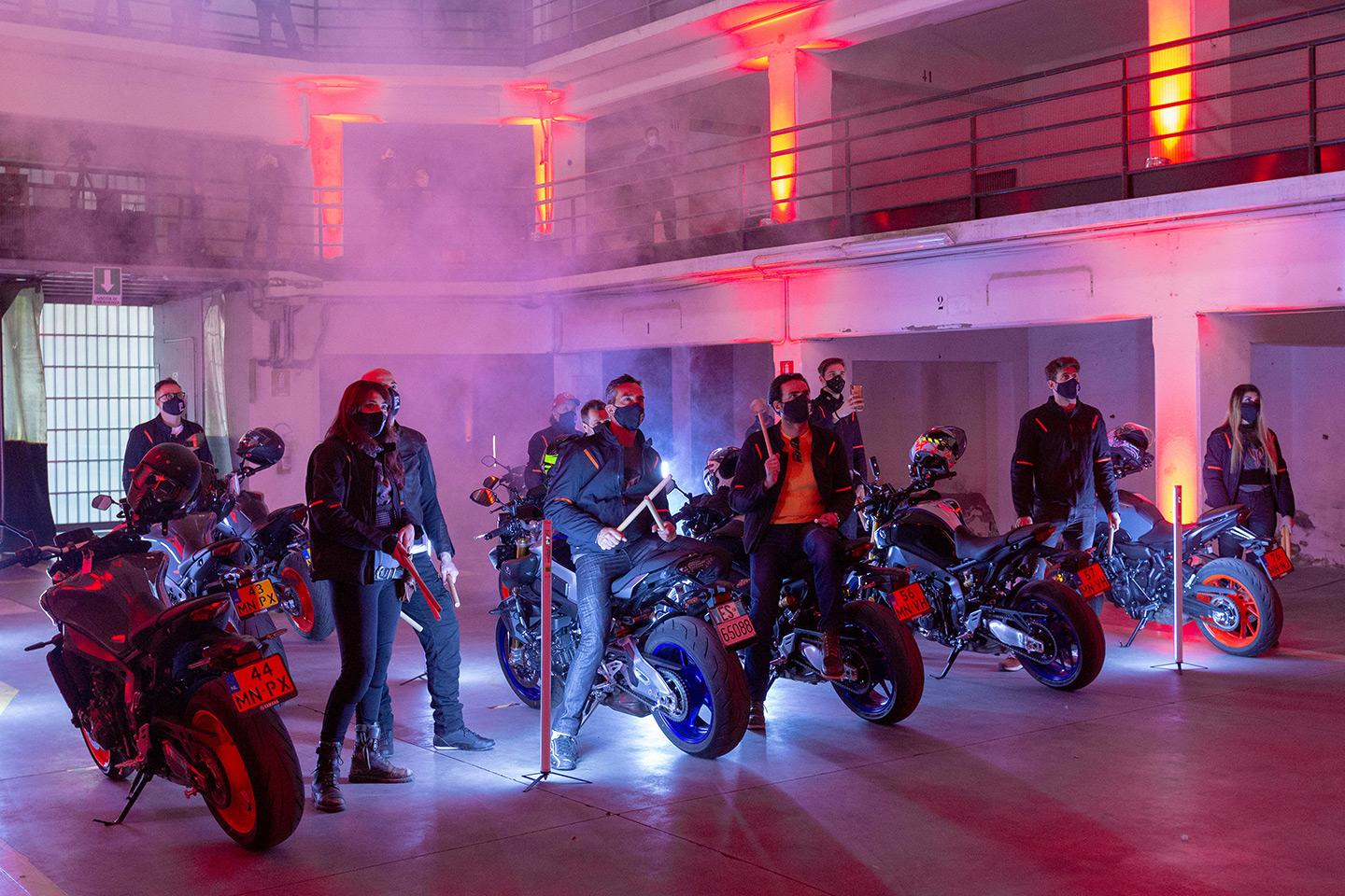 Modelli biker a fianco delle loro moto Yamaha in uno sfondo illuminato di viola, rosso e blu con fumogeni