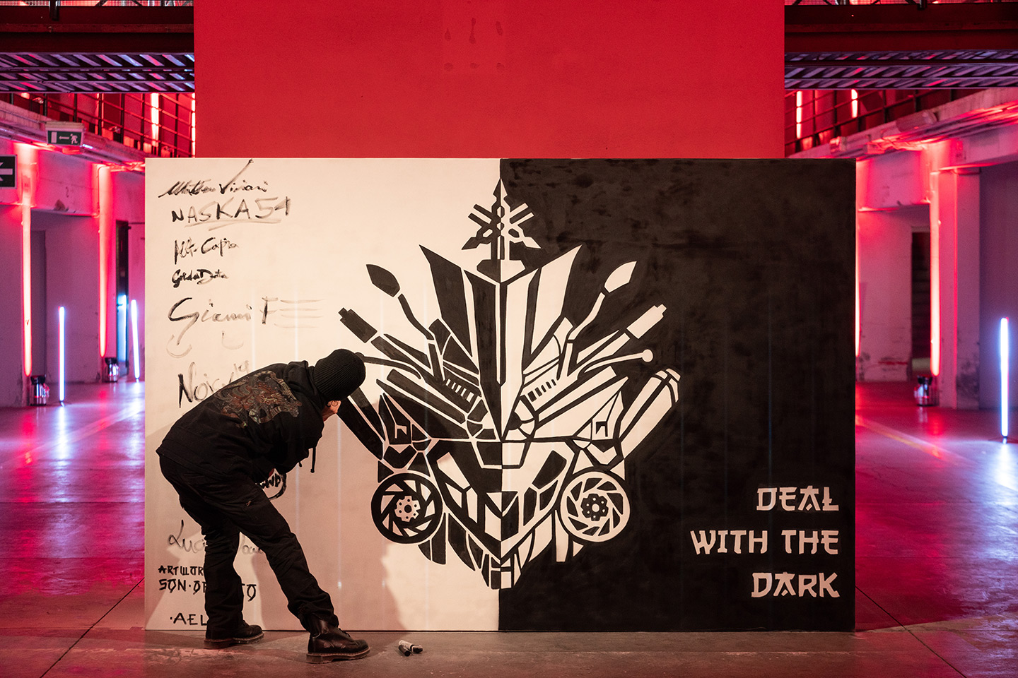 Street Artist che dipinge un murales in bianco e nero, realizzato per yamaha raffigurante lofo e componenti principali delle moto. In basso scrive "deal with the dark"