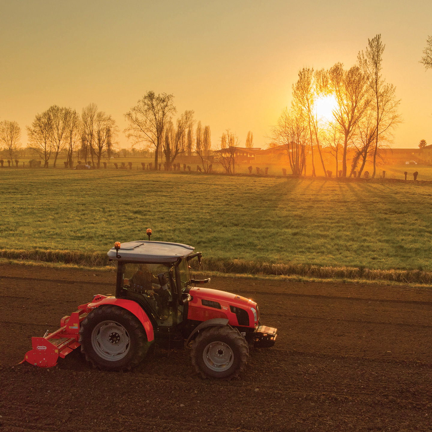 Trattore rosso SAME che lavora nei campi e nello sfondo il sole che tramotna